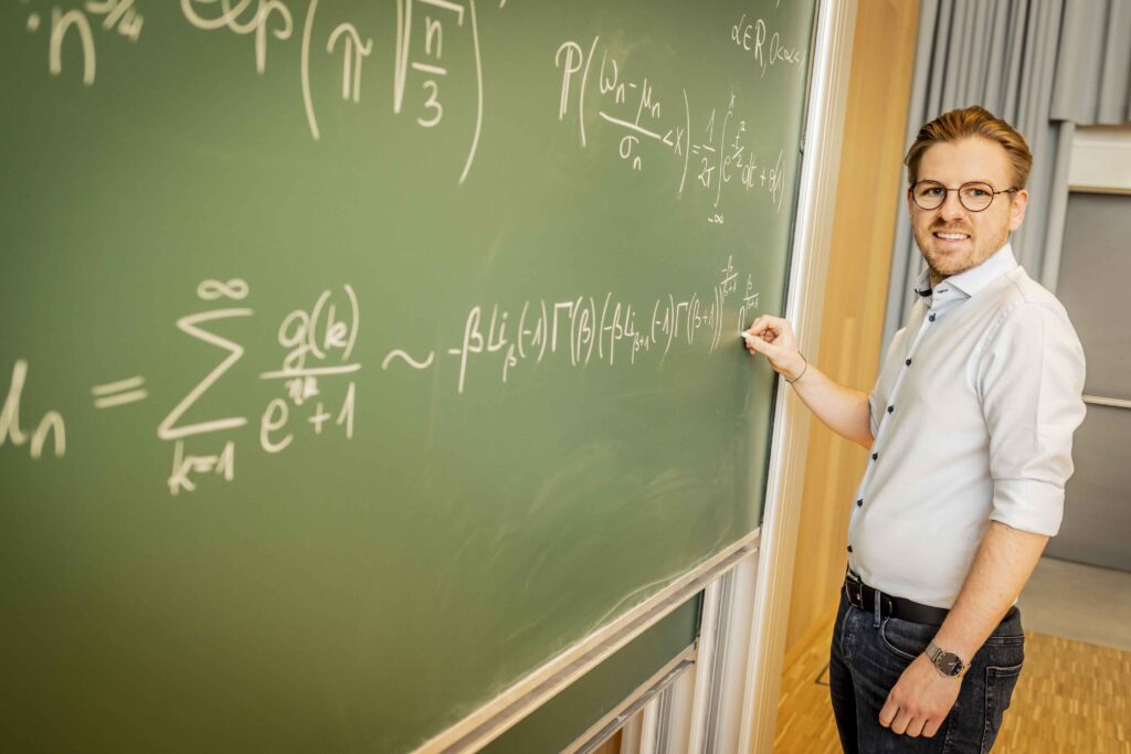 Foto von Gabriel Lipnik vor einer Tafel mit mathematischen Gleichungen